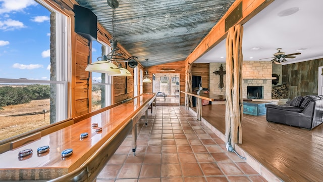 interior space featuring vaulted ceiling, a stone fireplace, wooden walls, tile patterned flooring, and ceiling fan