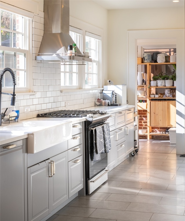 kitchen featuring stainless steel range with gas cooktop, white cabinetry, wall chimney range hood, and backsplash