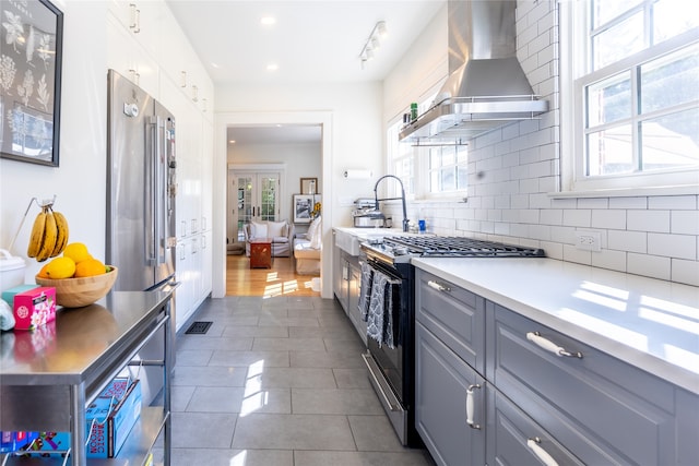 kitchen with wall chimney range hood, appliances with stainless steel finishes, plenty of natural light, and gray cabinets