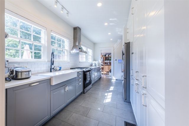 kitchen featuring wall chimney range hood, decorative backsplash, sink, gray cabinetry, and stainless steel appliances