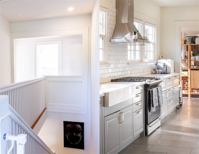 kitchen featuring decorative backsplash, wall chimney range hood, stainless steel gas range, sink, and white cabinetry