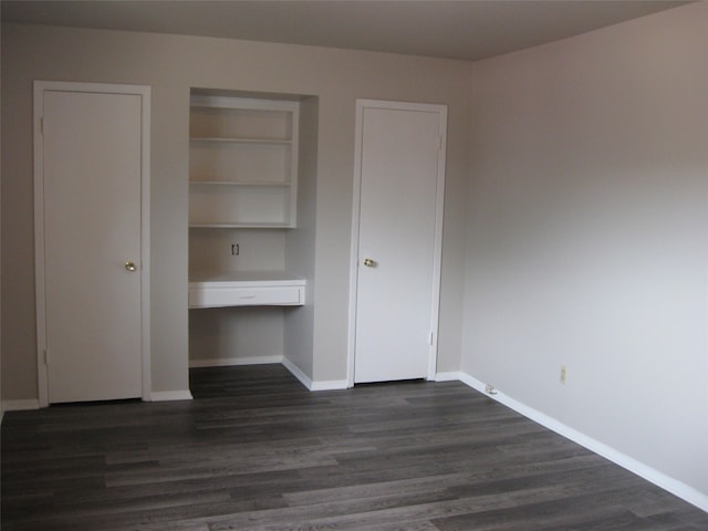 unfurnished bedroom with a closet, built in desk, and dark hardwood / wood-style floors