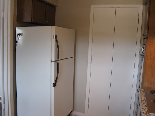 kitchen with dark brown cabinets, white cabinets, stovetop, and white fridge