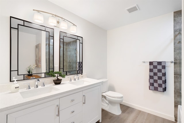 bathroom featuring vanity, tiled shower, hardwood / wood-style flooring, and toilet