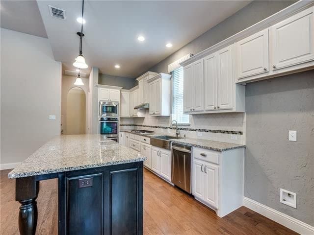 kitchen featuring white cabinetry, appliances with stainless steel finishes, decorative light fixtures, light stone countertops, and sink