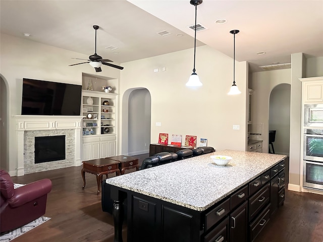 kitchen featuring stainless steel appliances, dark hardwood / wood-style floors, a stone fireplace, a center island, and pendant lighting