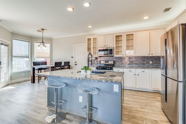 kitchen with a breakfast bar, a center island with sink, appliances with stainless steel finishes, decorative light fixtures, and light stone counters