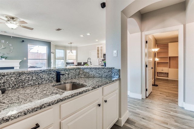 kitchen with light stone countertops, light wood-type flooring, sink, pendant lighting, and white cabinets