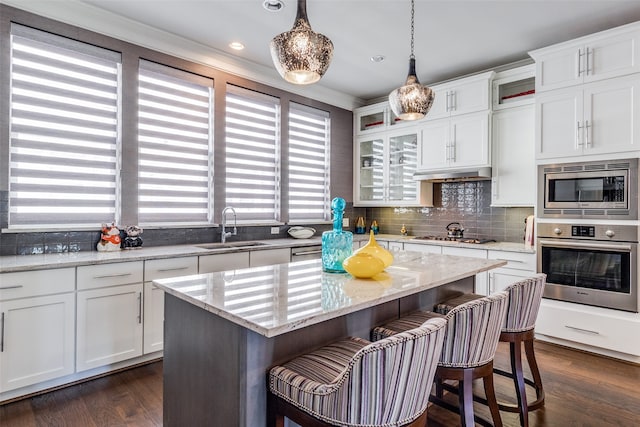 kitchen with stainless steel appliances, sink, a center island, white cabinetry, and light stone counters