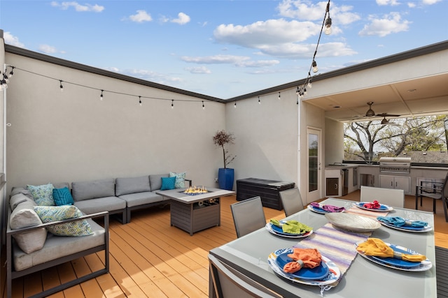 deck with ceiling fan, grilling area, an outdoor living space with a fire pit, and exterior kitchen