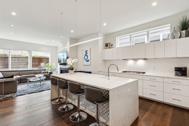 kitchen with a kitchen breakfast bar, white cabinetry, a kitchen island with sink, and dark hardwood / wood-style floors