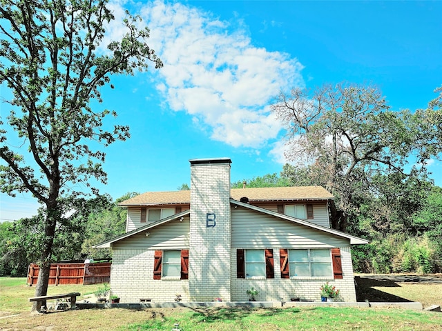 rear view of property featuring brick siding, a chimney, and fence