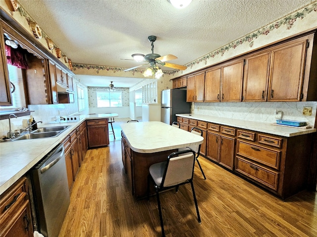 kitchen with sink, a textured ceiling, appliances with stainless steel finishes, dark hardwood / wood-style floors, and a kitchen bar