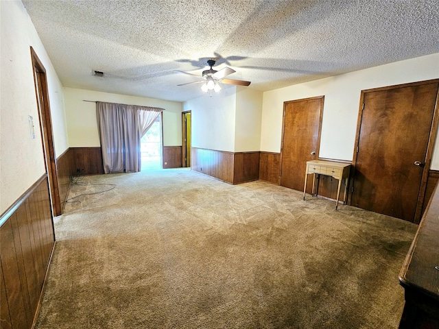 carpeted spare room with ceiling fan, wood walls, and a textured ceiling