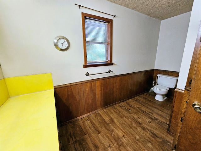 bathroom with hardwood / wood-style flooring, wood walls, toilet, and a textured ceiling