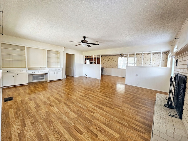 unfurnished living room with ceiling fan, a textured ceiling, a fireplace, and light wood-type flooring