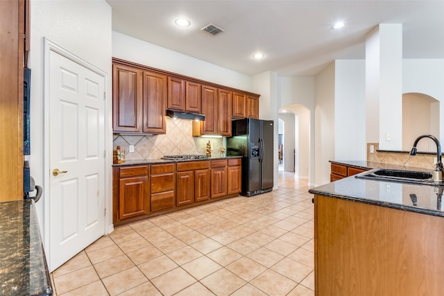 kitchen with decorative backsplash, sink, black fridge, dark stone counters, and light tile patterned floors