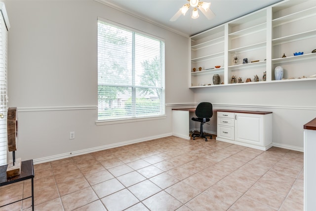 unfurnished office featuring ceiling fan, built in desk, light tile patterned floors, and crown molding