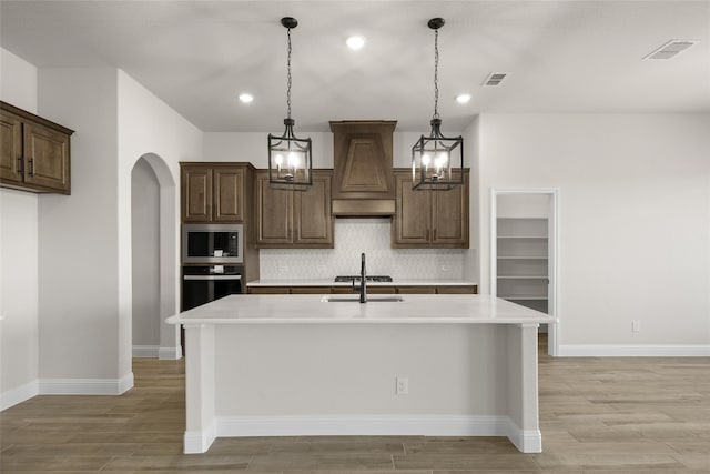 kitchen with tasteful backsplash, oven, light hardwood / wood-style flooring, a center island with sink, and built in microwave