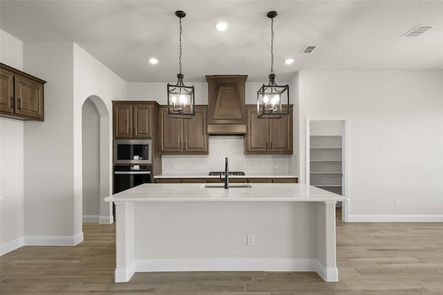 kitchen featuring a center island with sink, stainless steel appliances, decorative backsplash, custom range hood, and sink