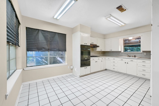 kitchen with light tile patterned flooring, white cabinets, tasteful backsplash, and oven