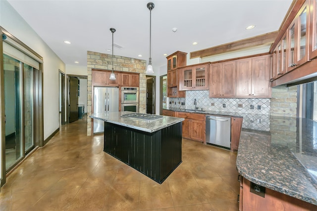 kitchen with dark stone counters, a kitchen island, sink, stainless steel appliances, and hanging light fixtures