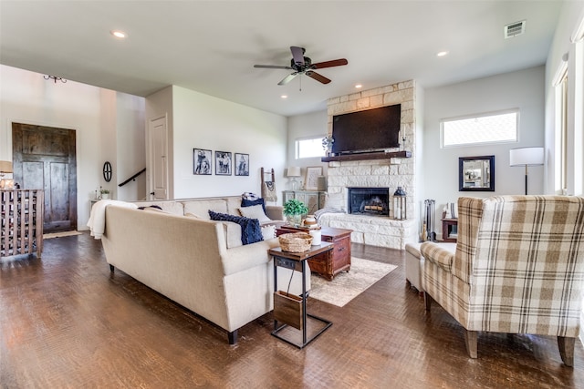 living room featuring a stone fireplace, dark wood-type flooring, and ceiling fan