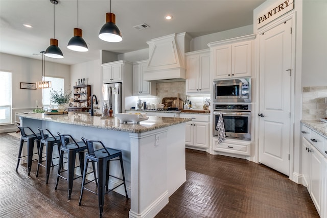 kitchen with a center island with sink, appliances with stainless steel finishes, light stone countertops, and white cabinetry