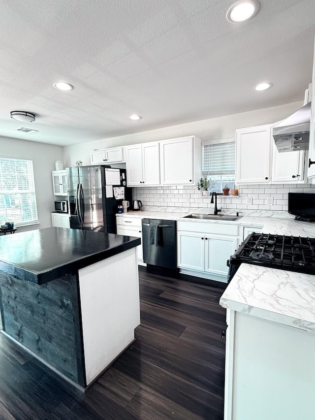 kitchen with white cabinetry, sink, stainless steel fridge, dishwashing machine, and wall chimney range hood