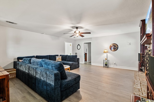 living room with a textured ceiling, ceiling fan, and light hardwood / wood-style flooring