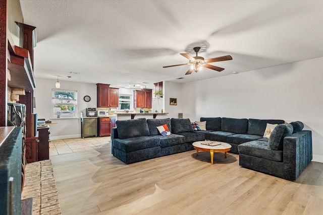 living room with ceiling fan, a textured ceiling, and light hardwood / wood-style flooring