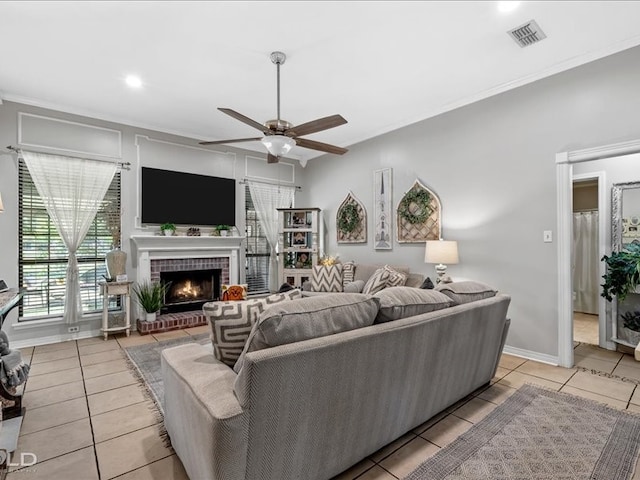 living room with ceiling fan, ornamental molding, a fireplace, and light tile patterned floors