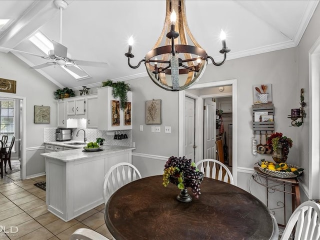 dining area with light tile patterned flooring, vaulted ceiling with skylight, ceiling fan with notable chandelier, and sink