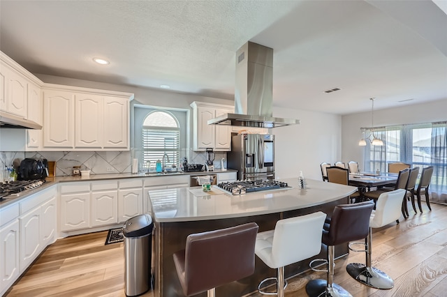 kitchen featuring island exhaust hood, light hardwood / wood-style flooring, hanging light fixtures, white cabinets, and appliances with stainless steel finishes