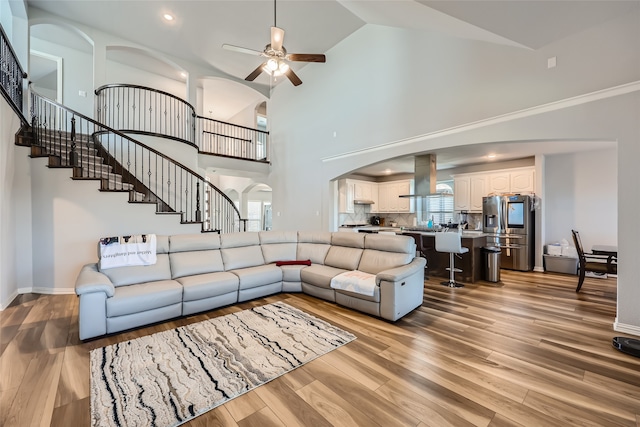 living room with high vaulted ceiling, ceiling fan, and light hardwood / wood-style flooring