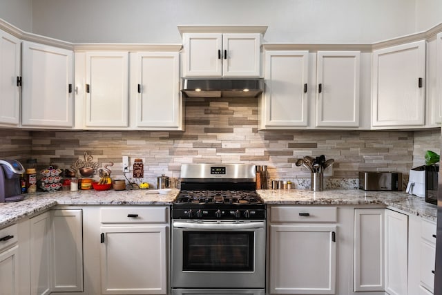 kitchen featuring decorative backsplash, light stone counters, stainless steel gas range oven, and white cabinetry