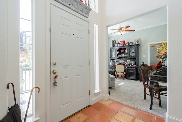 carpeted entrance foyer with ceiling fan, ornamental molding, and a healthy amount of sunlight