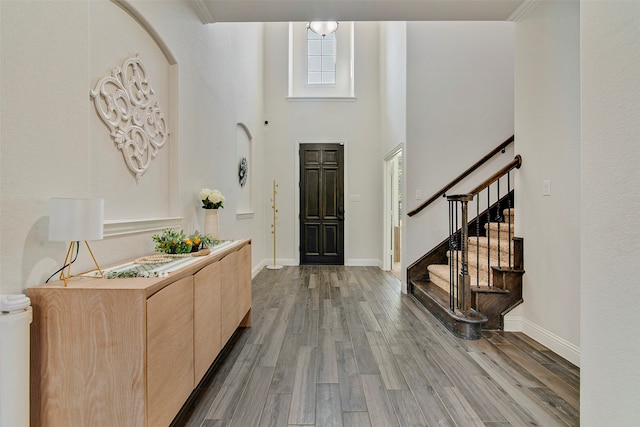 entryway with wood-type flooring, ornamental molding, and a towering ceiling