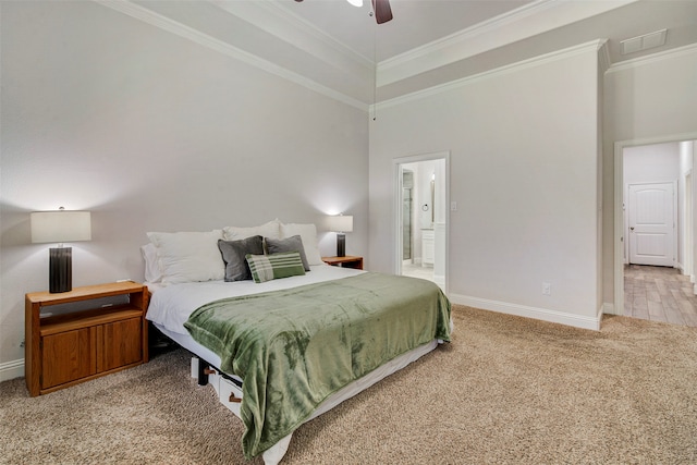 carpeted bedroom with ensuite bath, ceiling fan, crown molding, and a high ceiling