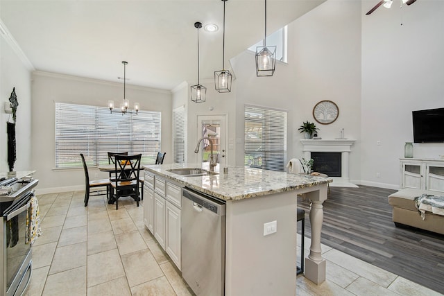 kitchen featuring appliances with stainless steel finishes, light wood-type flooring, sink, hanging light fixtures, and an island with sink