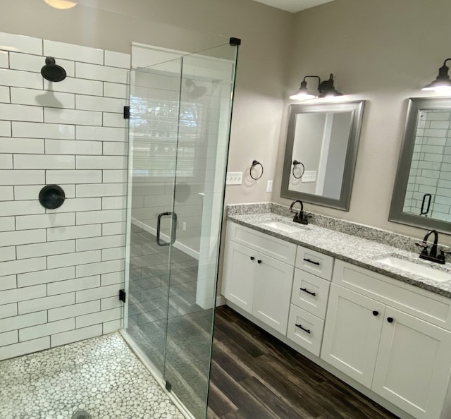 full bathroom featuring a sink, double vanity, a stall shower, and wood finished floors