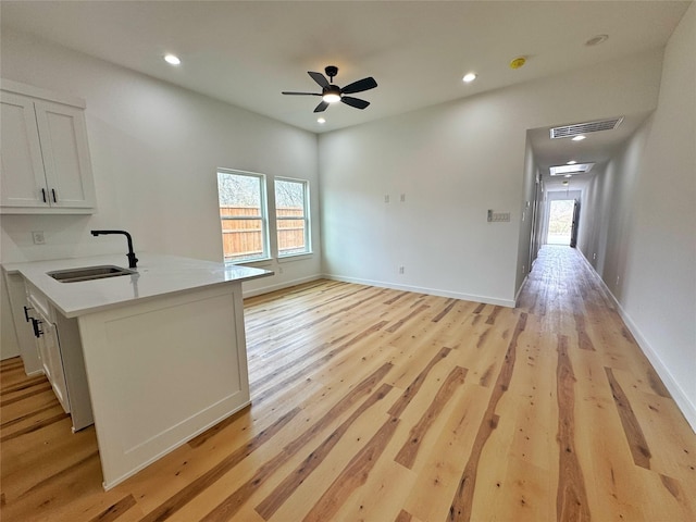 kitchen with light countertops, a sink, white cabinets, light wood-style floors, and ceiling fan