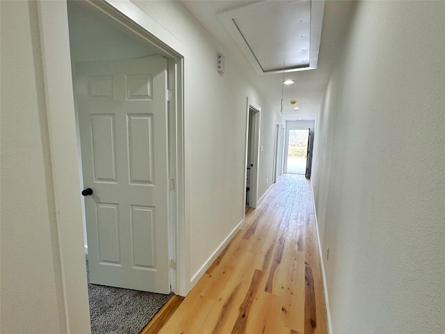 hall with light wood-style flooring, attic access, and baseboards