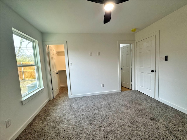 unfurnished bedroom featuring carpet, a walk in closet, a closet, ceiling fan, and baseboards