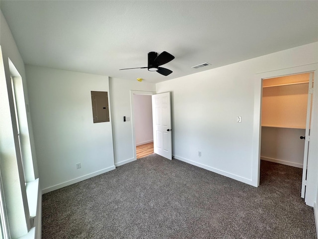unfurnished bedroom featuring electric panel, a spacious closet, dark colored carpet, baseboards, and visible vents