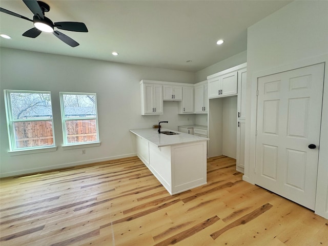 kitchen featuring white cabinets, a peninsula, light wood-type flooring, a sink, and recessed lighting