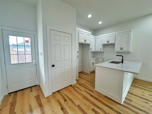 kitchen with a peninsula, light wood-type flooring, white cabinetry, and a sink