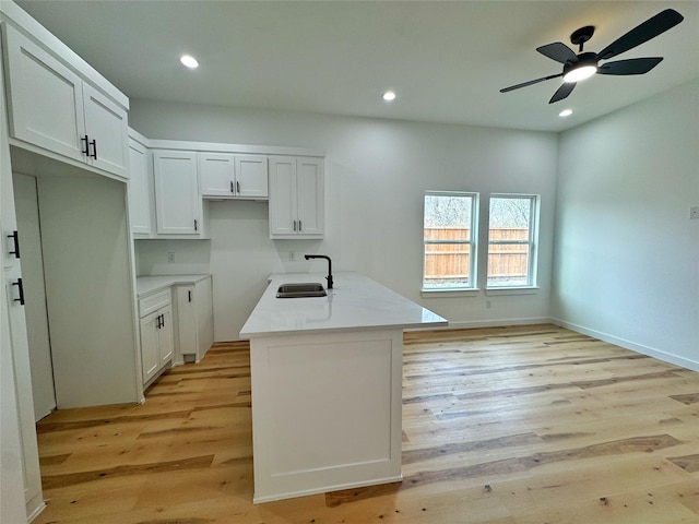 kitchen with light countertops, light wood-style floors, white cabinetry, a sink, and recessed lighting