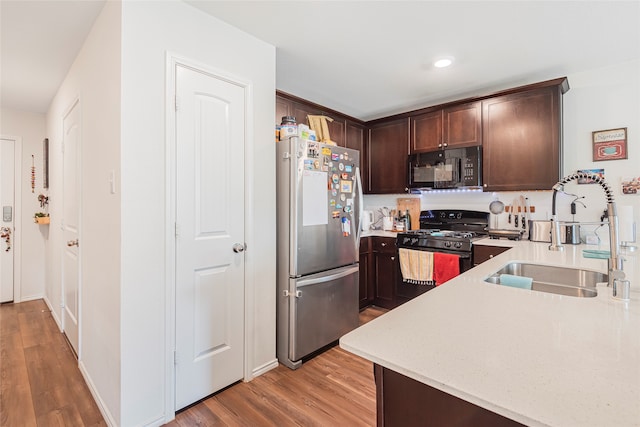 kitchen with black appliances, dark brown cabinetry, sink, and light hardwood / wood-style floors