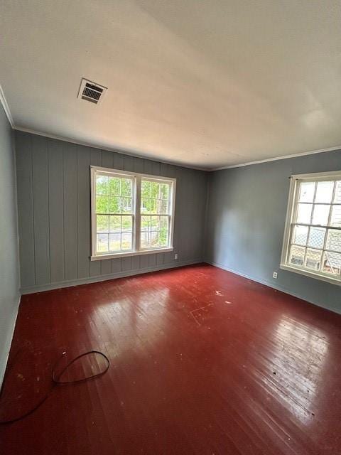 spare room featuring visible vents, ornamental molding, wood finished floors, and a wealth of natural light